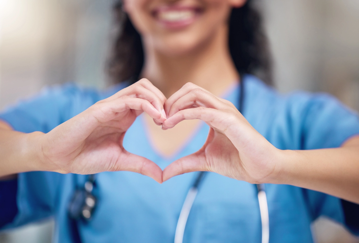 BD Medical Writing & Consulting - Glückliche Ärztin mit herzförmigen Händen als Zeichen der Liebe im Gesundheitswesen oder in der Lebensversicherung im Krankenhaus. Weibliche Person oder medizinische Fachkraft zeigt in der Klinik ein liebevolles Hand-Emoji, Symbol oder Zeichen.
